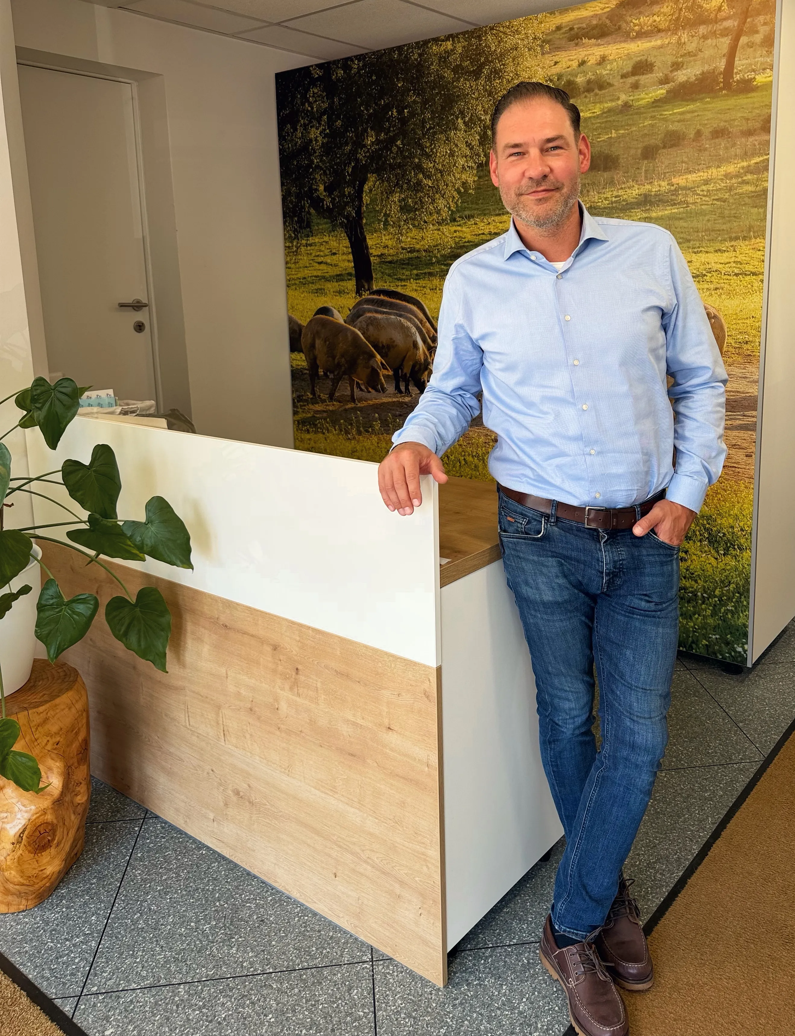 Christian Görisch lehnt am Empfang seiner Ordination in Sattledt, hinter ihm das Wandbild mit Weideschweinen